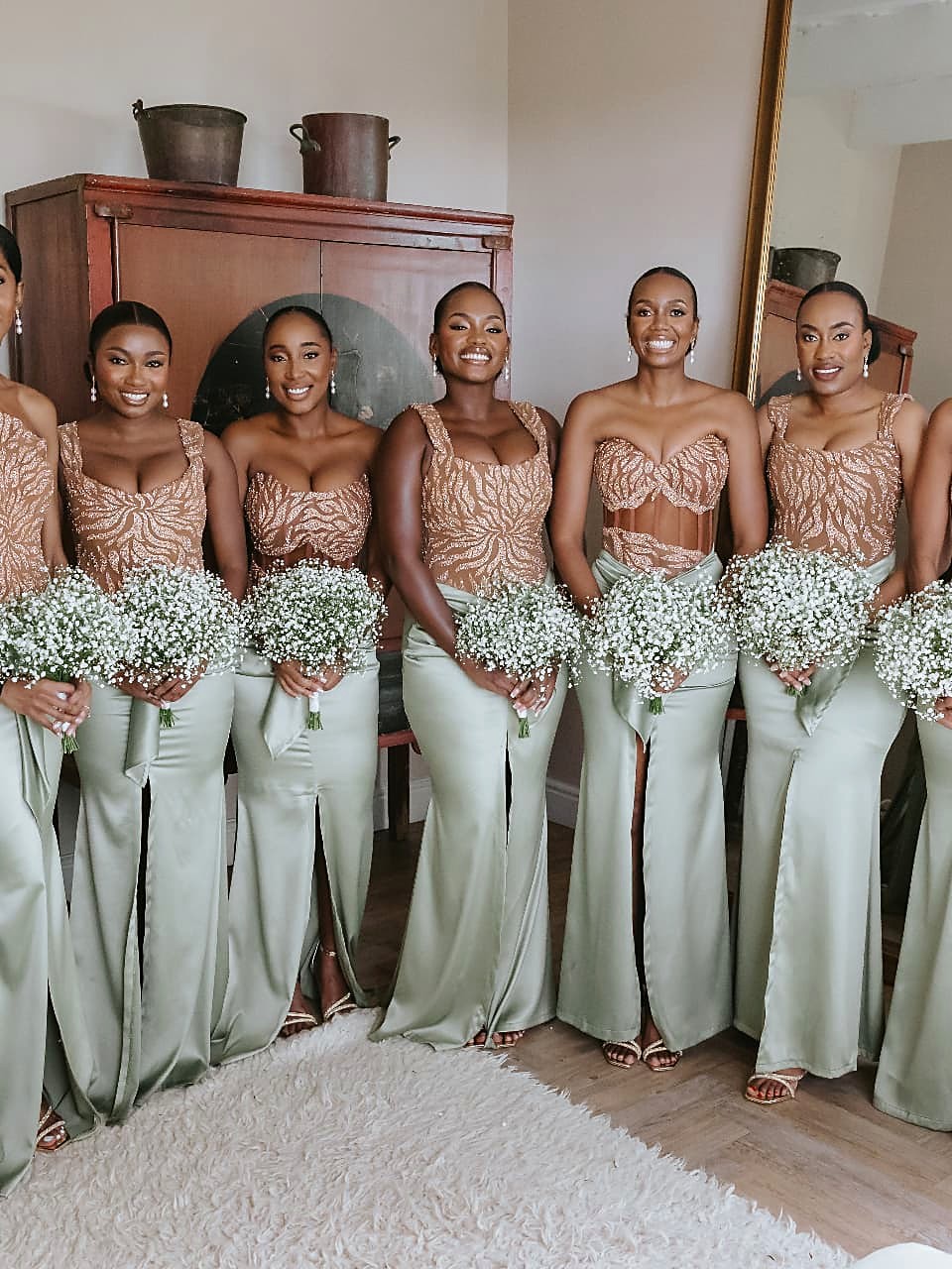 Nine bridesmaids in beaded copper bodices and sage green satin skirts holding gypsophila bouquets