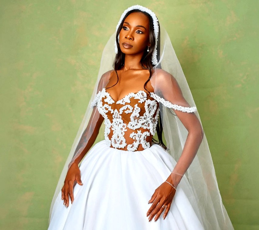 Bride in beaded corset gown with pearl-trimmed veil against a sage backdrop