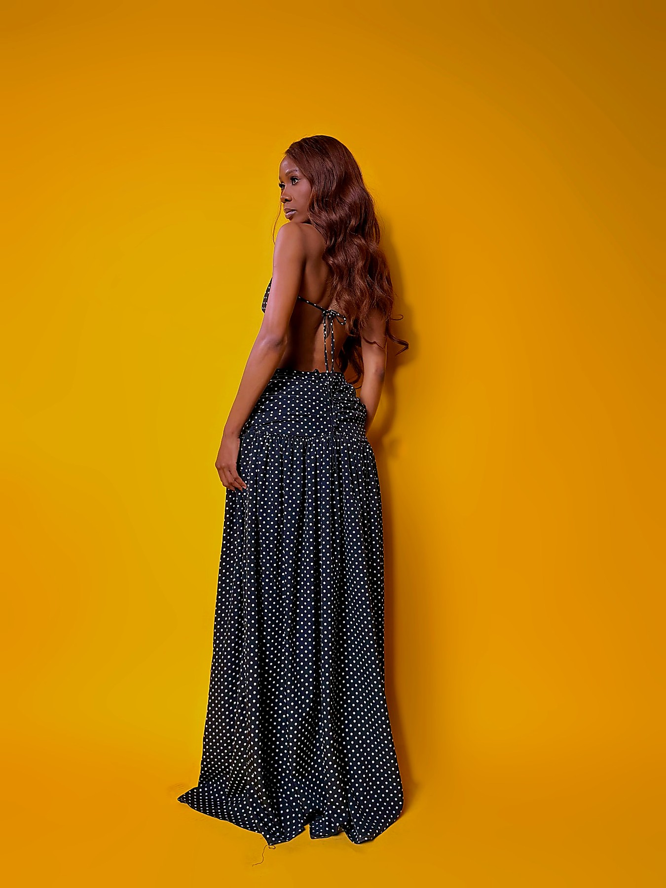 Open tie-back of the polka dot chiffon maxi, shot against a saffron backdrop